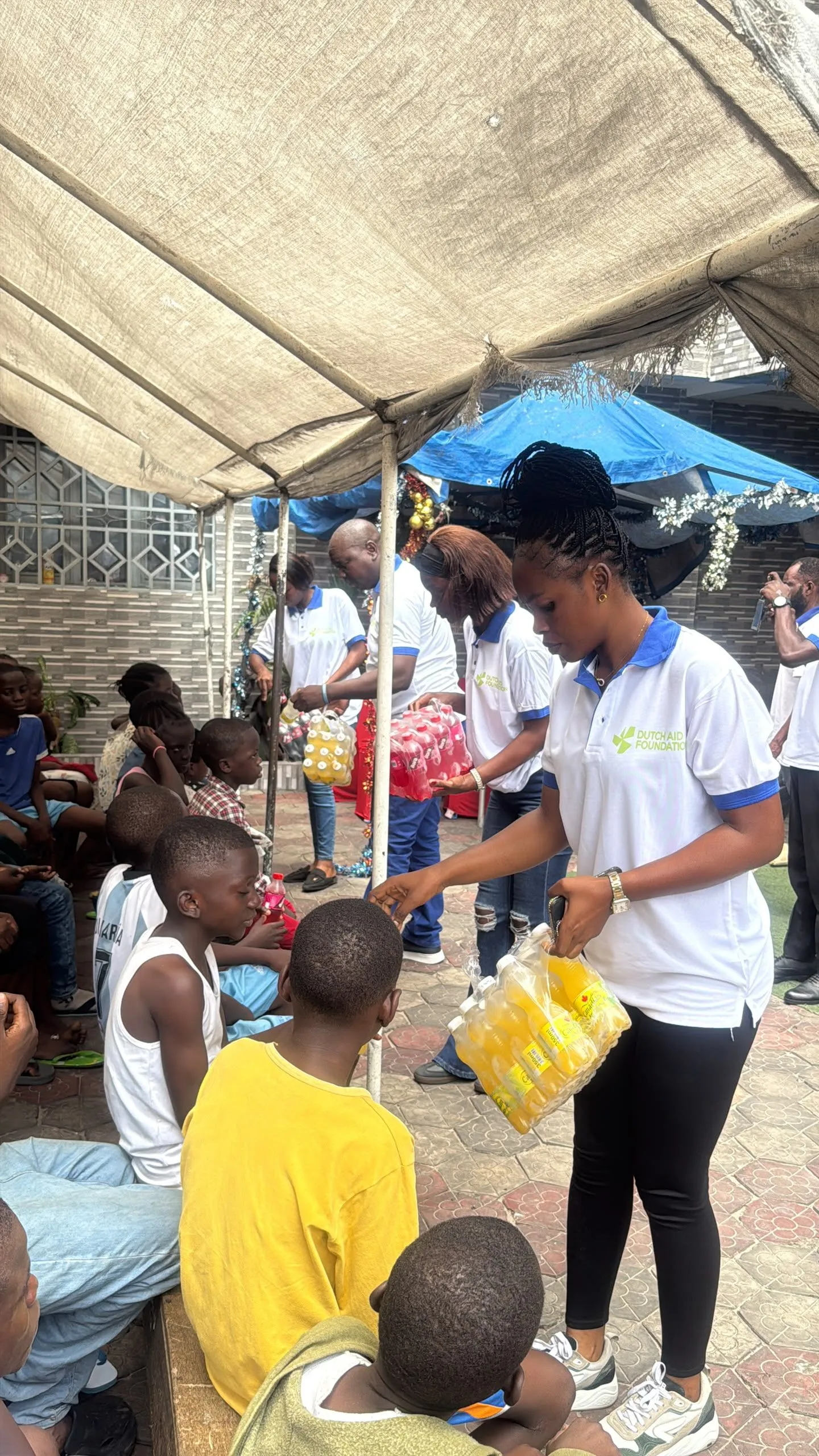 Een medewerker van Dutch Aid Foundation deelt flesjes drinken uit aan kinderen die onder een tent zitten in Congo.
