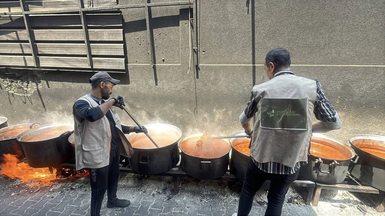 Twee veldmedewerkers van Dutch Aid Foundation bereiden warme maaltijden in grote pannen boven open vuur in Gaza.