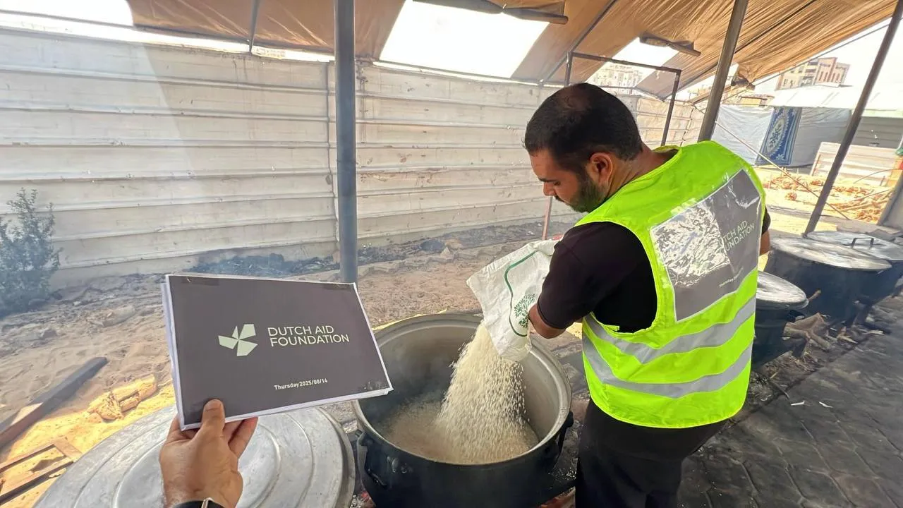 Een veldmedewerker van Dutch Aid Foundation giet rijst in een grote kookpan in Gaza.